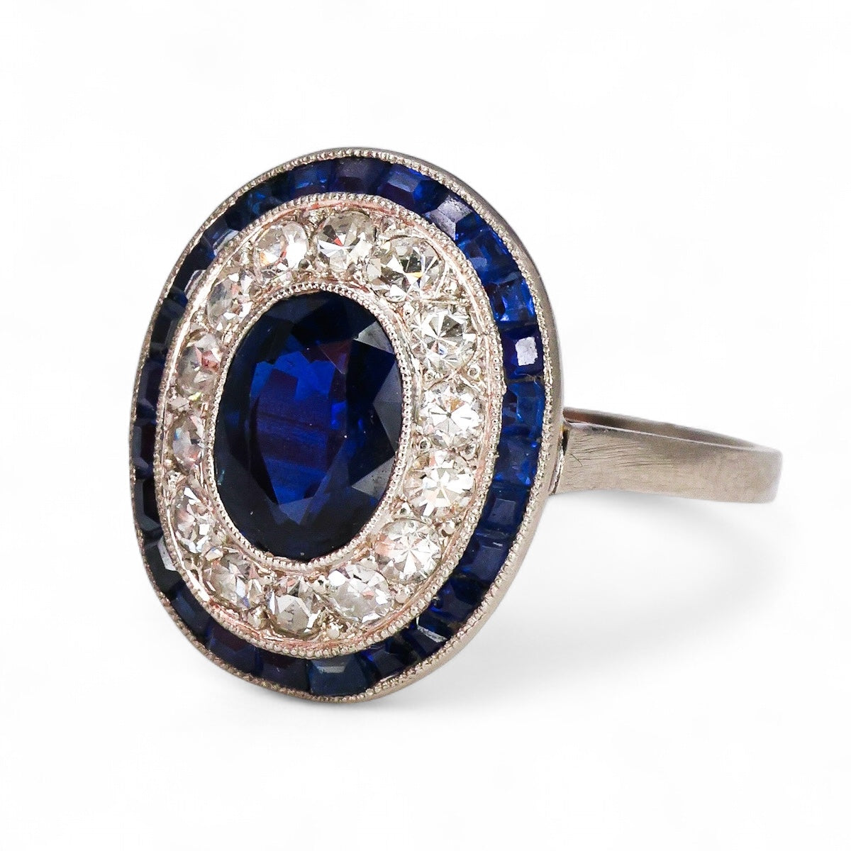 A very fine Platinum, Diamond & Sapphire Oval Target Ring, centrally Rub-over set with an Unheated Burma Sapphire. French. Circa 1930.
