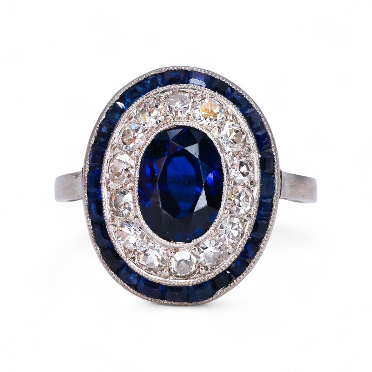 A very fine Platinum, Diamond & Sapphire Oval Target Ring, centrally Rub-over set with an Unheated Burma Sapphire. French. Circa 1930.